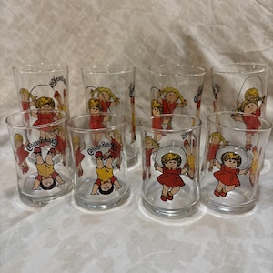 May include: A set of eight clear glass tumblers featuring Cabbage Patch Kids characters. Each glass displays colorful illustrations of children with yarn hair playing with jump ropes or performing handstands, accompanied by the Cabbage Patch Kids logo.