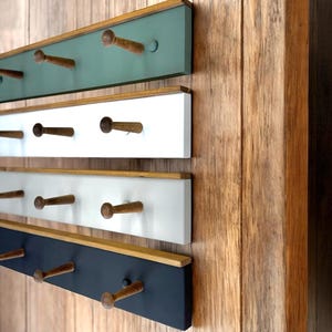 Peut inclure: Quatre porte-manteaux muraux en bois avec des panneaux de couleurs différentes. Le porte-manteau du haut est vert, le deuxième est blanc, le troisième est gris clair et le porte-manteau du bas est noir. Chaque porte-manteau a six chevilles en bois.
