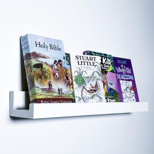 May include: A white shelf with five books on it. The books are "Holy Bible", "Stuart Little", "The Kid's Magic Club", "Diary of a Wimpy Kid: The Meltdown", and "The New Kid".