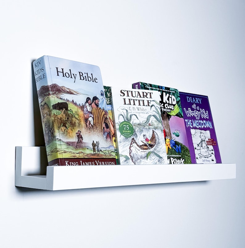 May include: A white shelf with five books on it. The books are "Holy Bible", "Stuart Little", "The Kid's Magic Club", "Diary of a Wimpy Kid: The Meltdown", and "The New Kid".