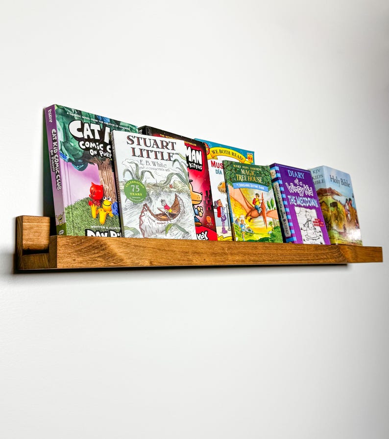 May include: A wooden shelf with a variety of children's books, including "Cat Kid Comic Club", "Stuart Little", "Magic Tree House", and "Diary of a Wimpy Kid".
