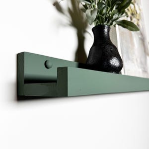 May include: A dark green wooden shelf with a rounded edge and a single screw visible on the front. The shelf is mounted to a white wall.