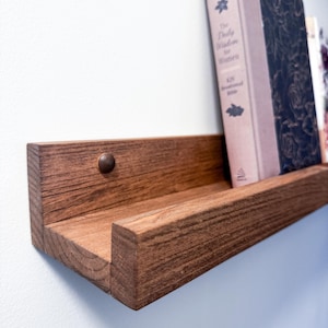 May include: A dark brown wooden shelf with a book titled "The Daily Wisdom for Women" resting on it.