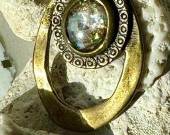 May include: A brass pendant necklace with a circular design featuring a clear iridescent stone. The pendant is attached to a chain with a light blue glass bead.