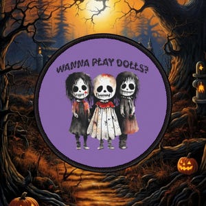 May include: A circular patch with the text "WANNA PLAY DOLLS?" features three stylized doll figures with skull-like faces and dark hair, dressed in black and red dresses. The background is a spooky Halloween scene.