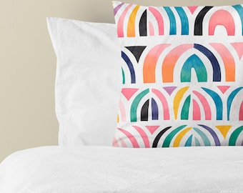 Puede incluir: Un cojín cuadrado con un patrón repetitivo de formas arqueadas en colores vibrantes que incluyen rosa, naranja, amarillo, azul verdoso, azul y negro sobre un fondo blanco. El diseño consiste en filas apiladas de motivos semicirculares.
