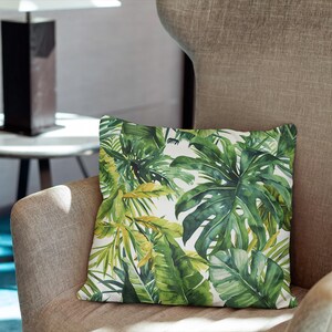 May include: A square throw pillow featuring a vibrant botanical print with various shades of green monstera and palm leaves set against a crisp white background, showcasing detailed foliage patterns across the entire surface.
