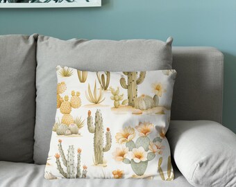 Puede incluir: Un cojín cuadrado con un patrón repetitivo de varios cactus y suculentas en tonos verde salvia, amarillo apagado y naranja suave sobre un fondo blanco, incluyendo cactus de nopal con flores en plena floración.
