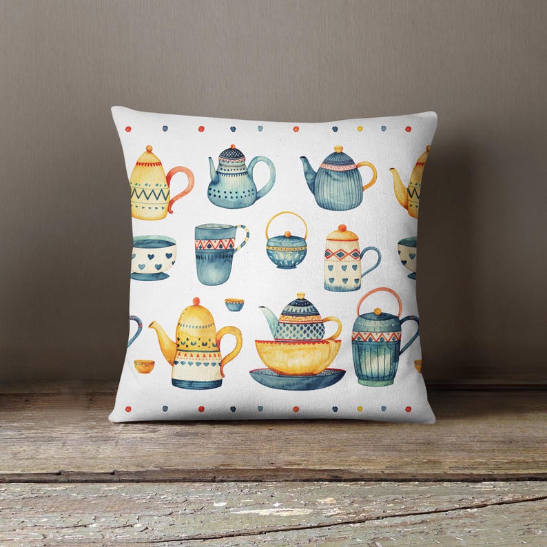 May include: A square throw pillow featuring a white background with a repeating watercolor pattern of various teapots, teacups, and bowls in shades of blue, yellow, and red, accented by a border of small colored dots along the top and bottom.