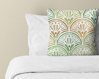 Puede incluir: Un cojín cuadrado con un patrón repetitivo en forma de abanico en tonos verdes y dorados sobre un fondo blanco. El diseño consiste en arcos semicirculares superpuestos con líneas verticales y puntos, creando un motivo decorativo simétrico.