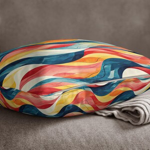 May include: A square throw pillow featuring a vibrant, abstract pattern of flowing, wavy lines in shades of deep blue, bright orange, soft yellow, and muted red. The fabric has a smooth texture with a visible seam running across the center.