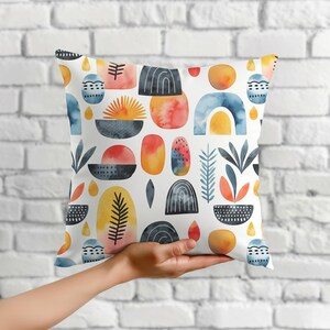 May include: A decorative throw pillow with a white background and a repeating watercolor pattern. The pattern features abstract shapes in shades of blue, orange, yellow, and black. The pillow is square and appears to be made of a soft fabric.