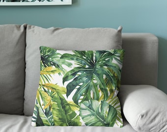 Puede incluir: Un cojín cuadrado con un vibrante estampado de acuarela de exuberantes hojas de monstera verdes y follaje tropical sobre un fondo blanco. El patrón botánico muestra varios tonos de verde bosque, lima y verde amarillento.