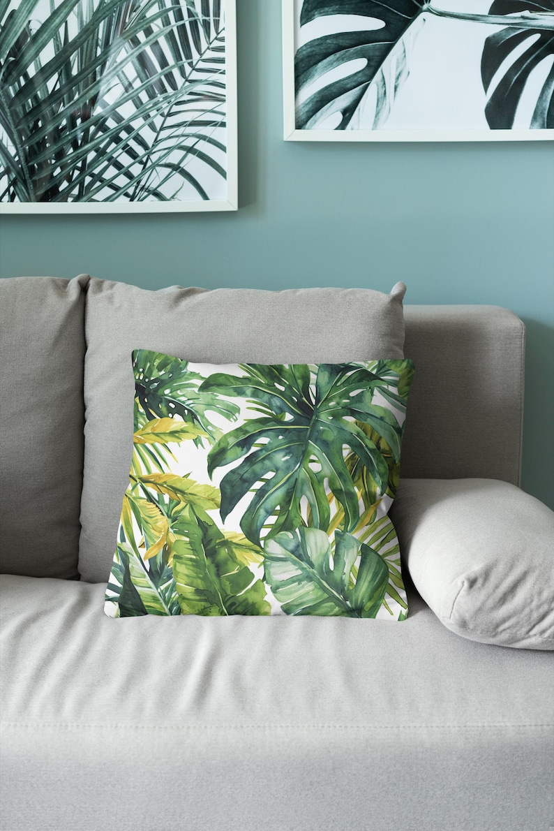 May include: A square throw pillow featuring a vibrant watercolor print of lush green monstera leaves and tropical foliage against a crisp white background. The botanical pattern displays various shades of deep forest green, lime, and yellow-green.