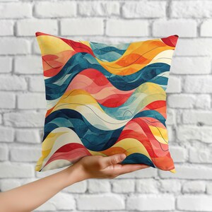 May include: A square throw pillow featuring a vibrant abstract pattern of flowing, wavy lines in shades of deep blue, bright yellow, soft pink, and warm orange, with thin black contour lines accentuating the fluid, layered design.