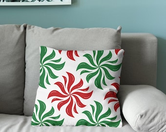 Puede incluir: Un cojín cuadrado con un patrón repetitivo de formas de molinillo en espiral estilizadas en colores rojo y verde alternos sobre un fondo blanco sólido. El diseño consta de múltiples pétalos curvos que irradian desde un punto central.