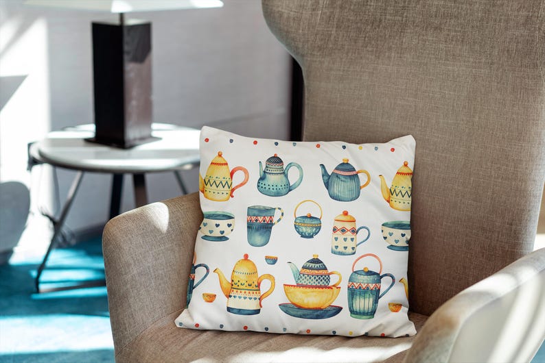 May include: A square throw pillow with a white background featuring a repeating watercolor pattern of various teapots, cups, and bowls in shades of blue, yellow, and orange, accented with small colorful dots along the top and bottom edges.