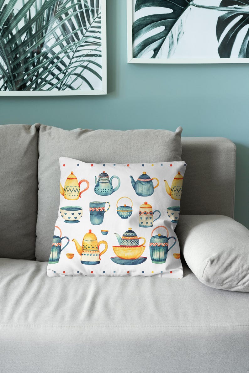 May include: A square throw pillow featuring a white background with a repeating pattern of various teapots, teacups, and bowls in shades of blue, yellow, and orange. The design includes small colorful dots along the top and bottom edges.