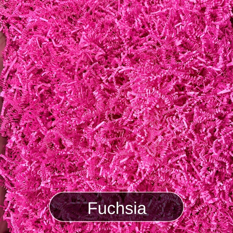 May include: A close-up of fuchsia-colored shredded paper, commonly used for packing and gift wrapping.