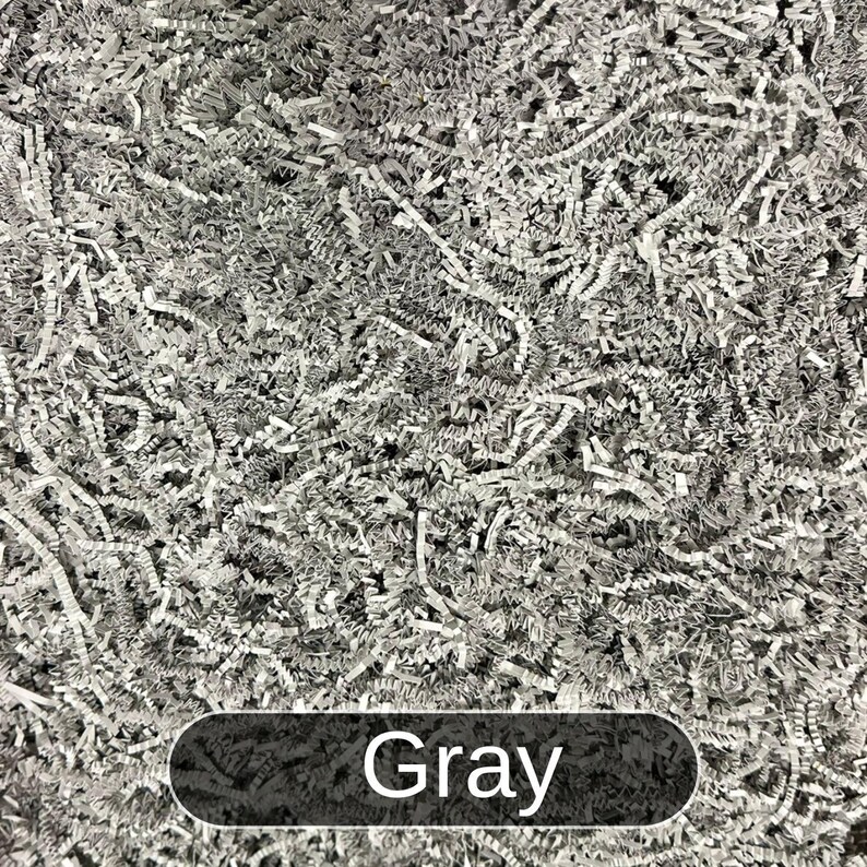 May include: Gray shredded paper filling a container. The paper is made of thin, crinkled strips.