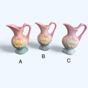 May include: Three vintage ceramic pitchers with floral designs in shades of pink, yellow, and green. The pitchers have a delicate, feminine style and are perfect for adding a touch of vintage charm to any home.