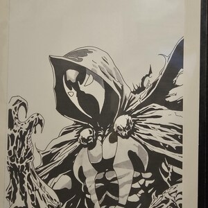 Op de afbeelding: Een zwart-witte inktillustratie van een figuur met een kap en masker, gekleed in een cape vastgemaakt met twee schedelvormige sluitingen. De figuur heeft &eacute;&eacute;n klauwhand naar voren uitgestoken. De handtekening Momoko '24 staat rechtsonder.