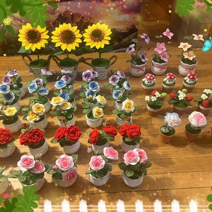 May include: A collection of crocheted flower arrangements in various colors, including red, pink, yellow, blue, and white. The flowers are displayed in small pots and feature different types of flowers, such as roses, sunflowers, and daisies.