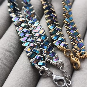 May include: Three beaded bracelets with iridescent blue and gold rectangular beads. The bracelets have silver and gold clasps. The beads are arranged in a woven pattern. The bracelets are displayed on a gray surface.