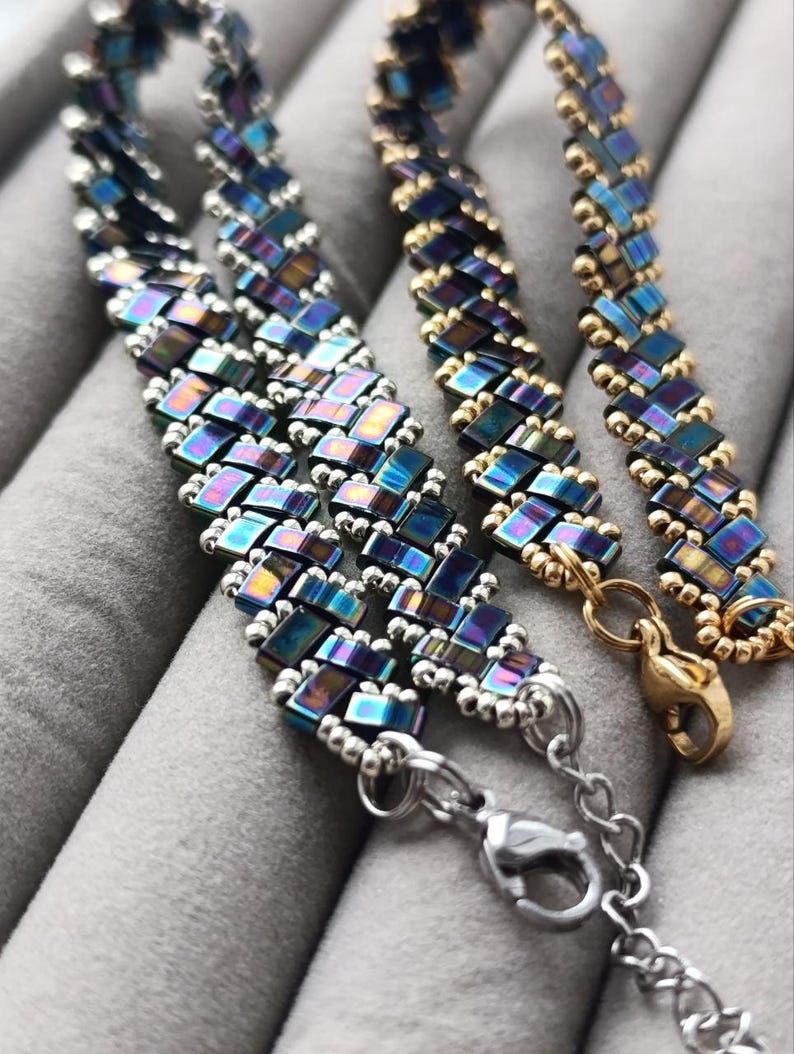 May include: Three beaded bracelets with iridescent blue and gold rectangular beads. The bracelets have silver and gold clasps. The beads are arranged in a woven pattern. The bracelets are displayed on a gray surface.