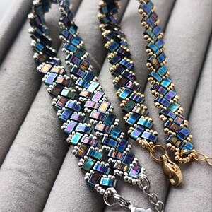 May include: Two beaded bracelets with iridescent blue, purple, and gold accents. One bracelet has silver-toned clasps and chain, while the other has gold-toned clasps. The bracelets are made of small, rectangular beads.