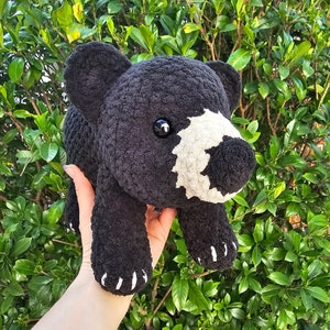 May include: A black and white crocheted stuffed animal bear with black eyes. The bear is being held in a person's hand.