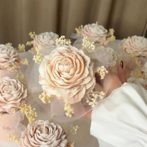 Può includere: Una collezione di piccole candele di colore crema a forma di fiore, con delicati dettagli in tulle bianco e respiro di bambino secco.