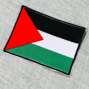 May include: A red, white, black, and green embroidered patch with a triangle shape in the top left corner. The patch is on a gray background.