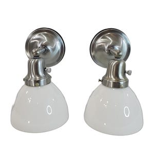 May include: A pair of silver wall sconces with white glass shades. The sconces have a simple, classic design and would be a great addition to any home.