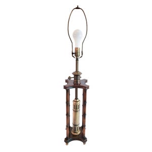 May include: An antique floor lamp with a dark wood base and a brass-colored metal center section. The lamp has a tall, slender design with a light bulb at the top. The lamp's base is a dark brown color.