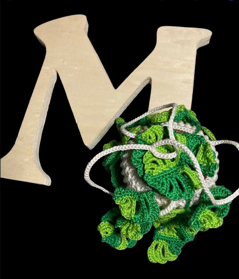 May include: A wooden letter M with a green and white crocheted ball of yarn with a white string attached.