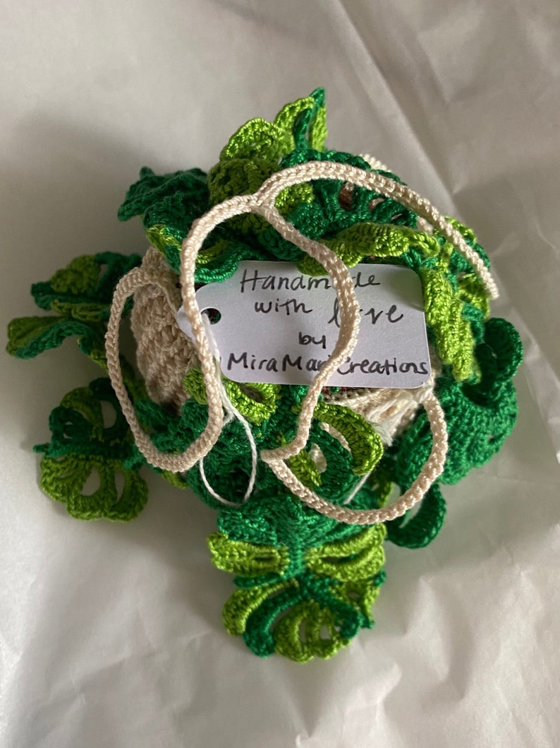 May include: A crocheted green and white plant with a tag that reads "Handmade with love by MiraMar Creations".