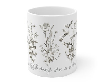Może przedstawiać: Biały kubek ceramiczny z czarno-białym wzorem kwiatowym i tekstem "We GROW through what we go through".