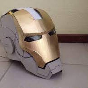 May include: A gold and white cardboard Iron Man helmet. The helmet has a detailed design with a gold faceplate and a white interior.