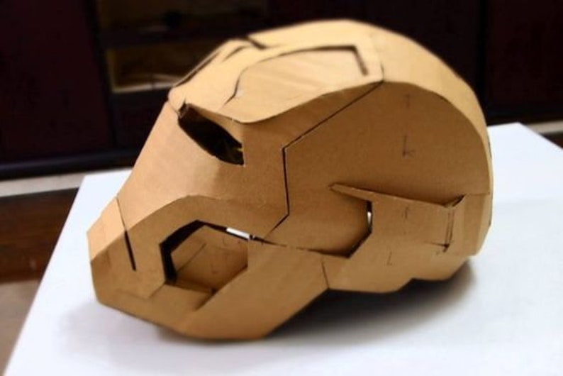 May include: A cardboard model of a helmet, possibly inspired by a superhero, with a brown color and intricate details.