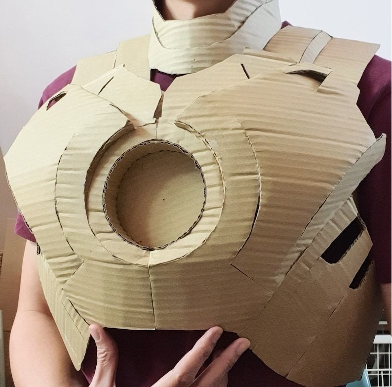 May include: A cardboard chest piece costume, resembling the Iron Man suit, with a circular opening in the center.