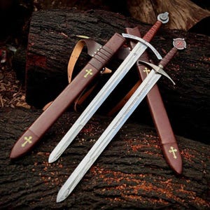 May include: Two medieval swords with silver blades and brown leather handles and sheaths. The sheaths have gold crosses. The swords are resting on a dark brown log.