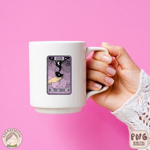 Pu&ograve; includere: Una tazza in ceramica bianca con un design di carta dei tarocchi viola che presenta un bicchiere di vino con una luna crescente e stelle al suo interno. La carta recita "XVIII THE WINE".