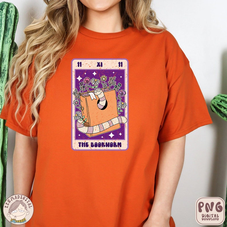 Puede incluir: Camiseta naranja con un gr&aacute;fico de un gusano de libro dentro de un libro con flores y estrellas. El gr&aacute;fico est&aacute; en estilo de carta de tarot con el n&uacute;mero 11 y el numeral romano XI. El texto "The Bookworm" est&aacute; debajo del gr&aacute;fico.