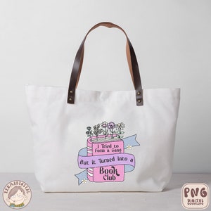 Puede incluir: Una bolsa de tela blanca con asas de cuero marr&oacute;n y un dise&ntilde;o rosa y azul con un libro con flores y el texto "Intent&eacute; formar una pandilla, pero se convirti&oacute; en un club de lectura".