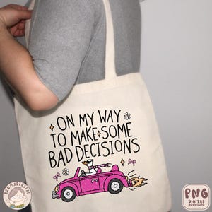 May include: A white tote bag featuring a pink car with a goose at the wheel. The text on the bag reads "On my way to make some bad decisions".