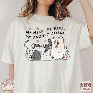 Puede incluir: Camiseta blanca con un gr&aacute;fico de un opossum con la boca abierta y el texto "My neck. My back. My anxiety attack."