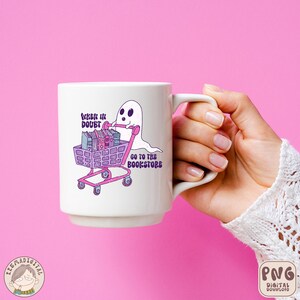 K&ouml;nnte beinhalten: Eine wei&szlig;e Keramiktasse mit einem Geist, der einen Einkaufswagen voller B&uuml;cher schiebt. Der Text auf der Tasse lautet "When in doubt, go to the bookstore".