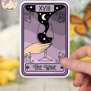Pu&ograve; includere: Una carta dei tarocchi viola con il numero XVIII e le parole "THE WINE" stampate su di essa. La carta raffigura una mano che tiene un bicchiere di vino con un liquido nero e stelle al suo interno. Il liquido si riversa dal bicchiere e forma una forma di mezzaluna.