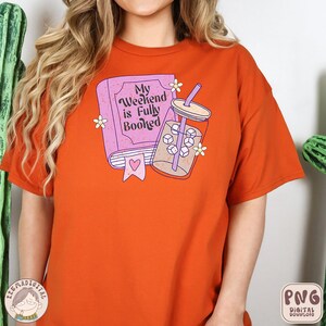 May include: Orange t-shirt with a pink book and a glass of iced coffee. The book has the text "My Weekend is Fully Booked".